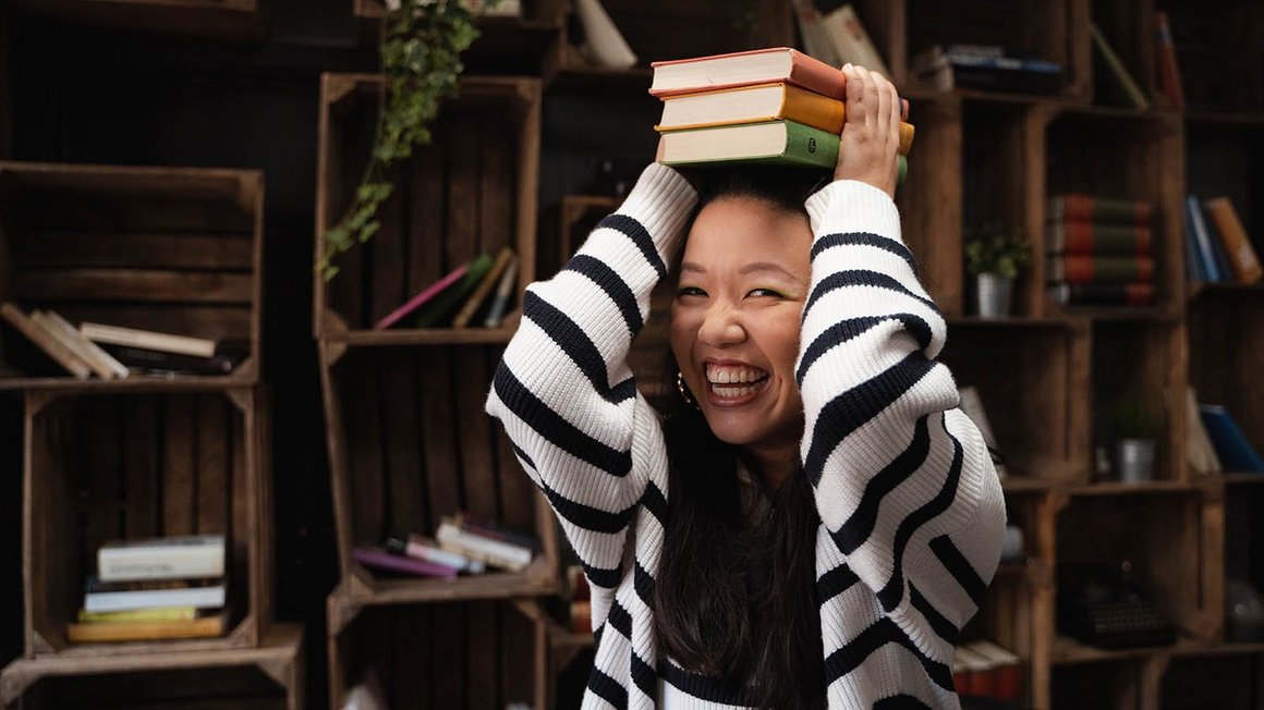 femme en pull raye tenant des livres au-dessus de sa tete en souriant.