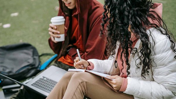 Kosten für Studiengebühren und Co. Zwei Studierende sitzen auf einer Wiese und lernen zusammen