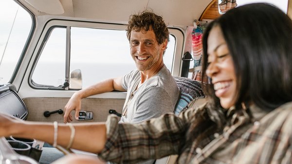 Junges Paar sitzt lächelnd am Steuer – Versicherungen für den Van