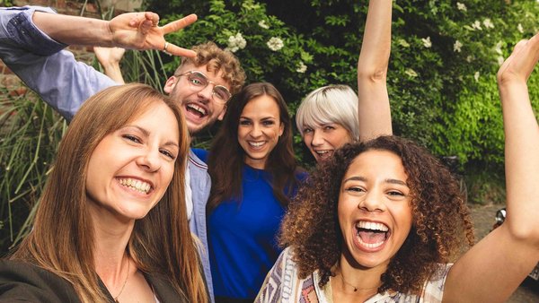 Planifier des vacances entre amis – voici comment faire Cinq amis se tiennent serres l'un contre l'autre et rient à la caméra