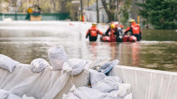 Dommages causes par les intemperies et leurs consequences financieres Sacs de sable avec des maisons inondees et une equipe de secours en arriere plan