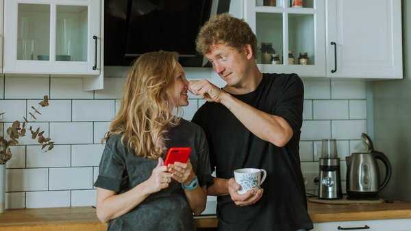 Frau und Mann stehen lachend in der Küche – gemeinsames Konto