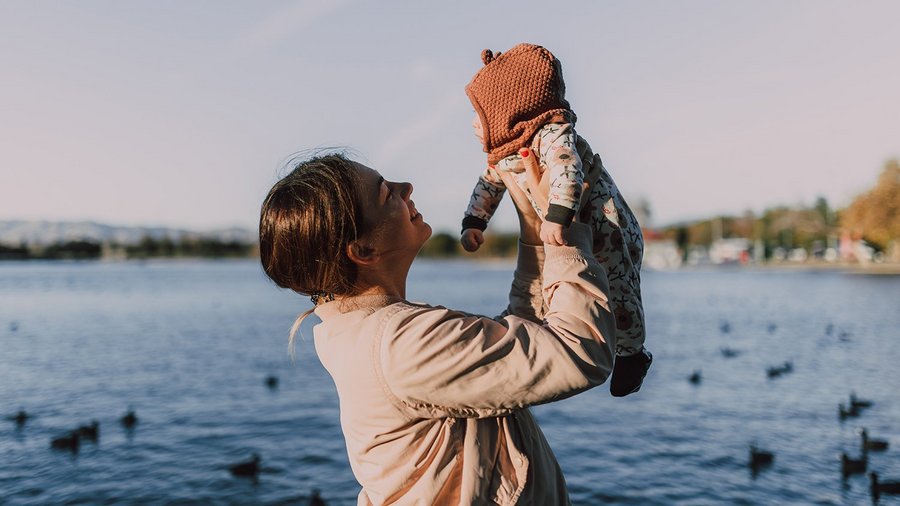 Une mere tient son bebe en l air devant un lac