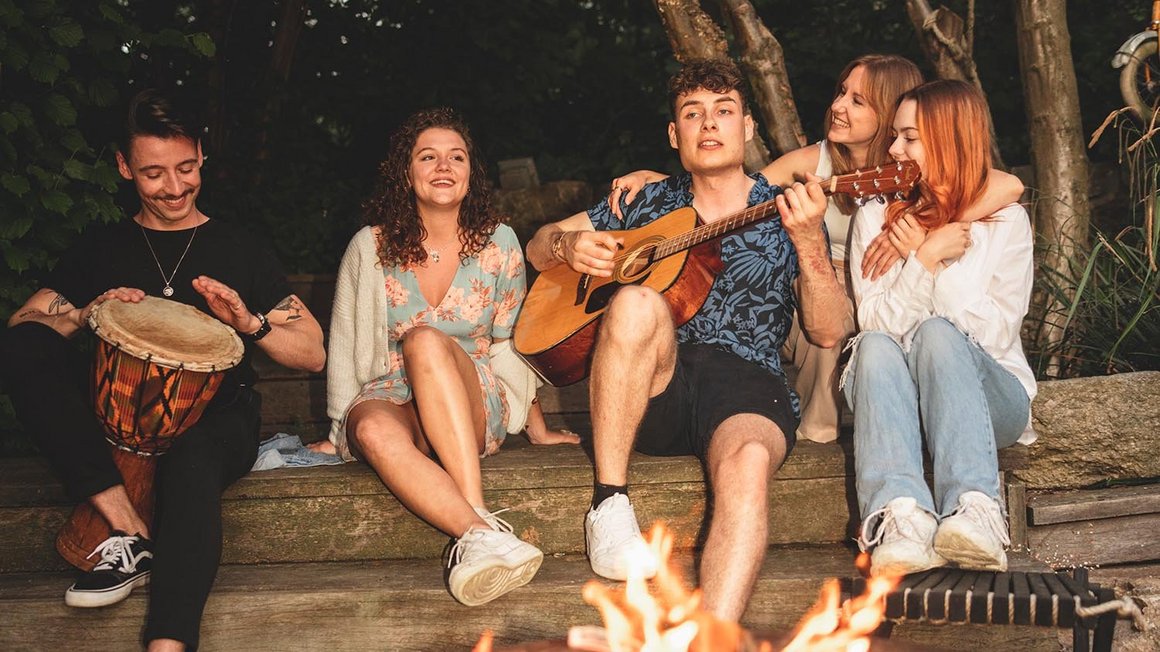 Quatre amis assis ensemble autour d'un feu de camp et jouant de la guitare