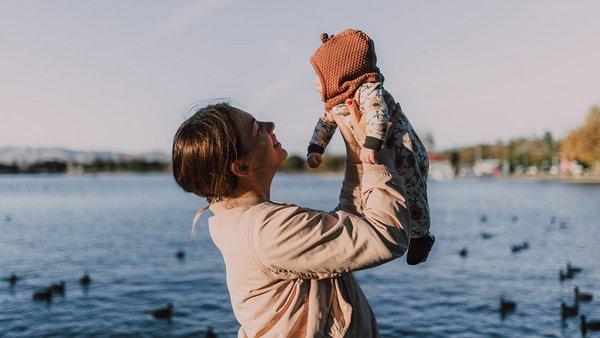 Mutter hält ihr Baby in der Luft vor einem See