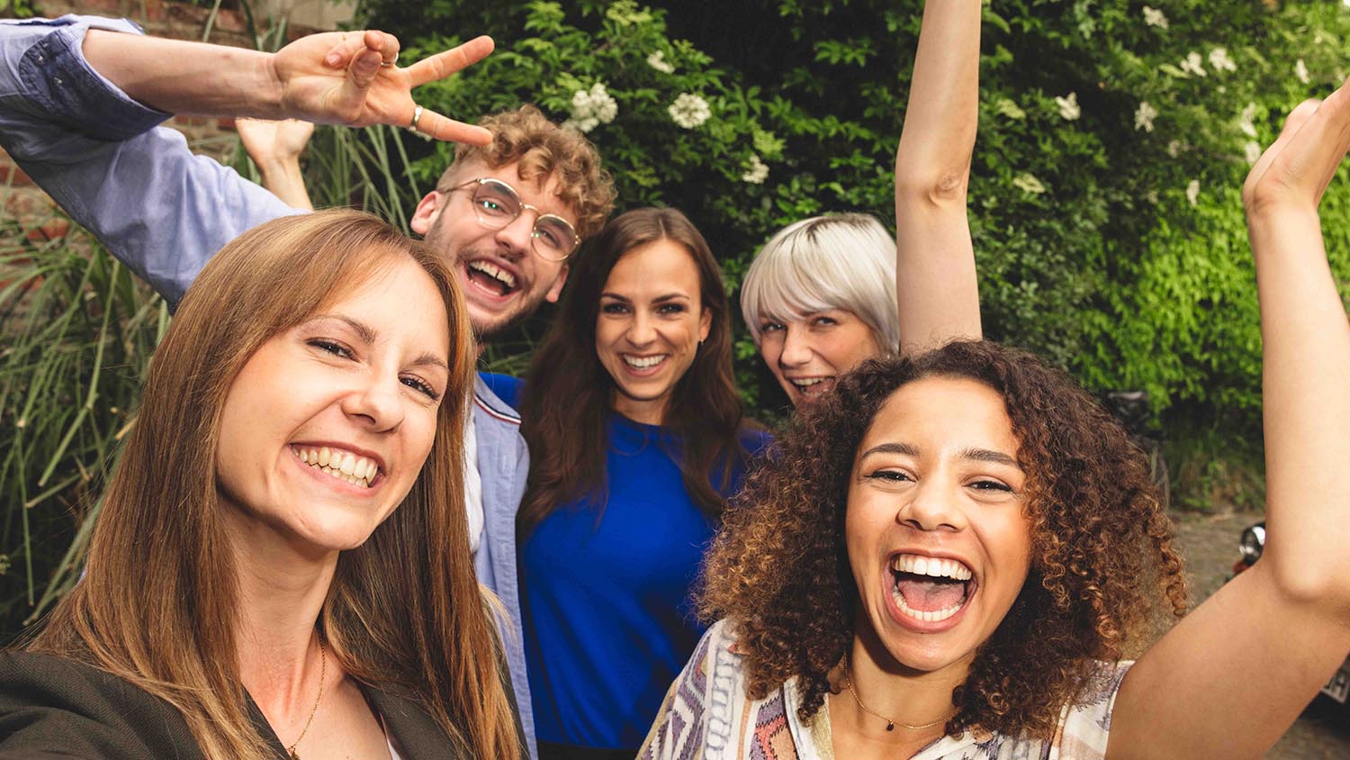 Planifier des vacances entre amis – voici comment faire Cinq amis se tiennent serres l'un contre l'autre et rient à la caméra