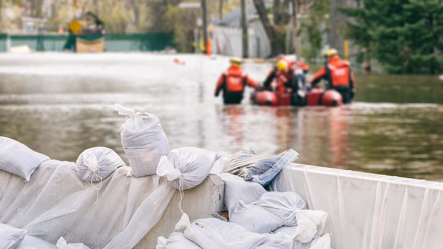 Sacs de sable avec des maisons inondees et une equipe de secours en arriere plan