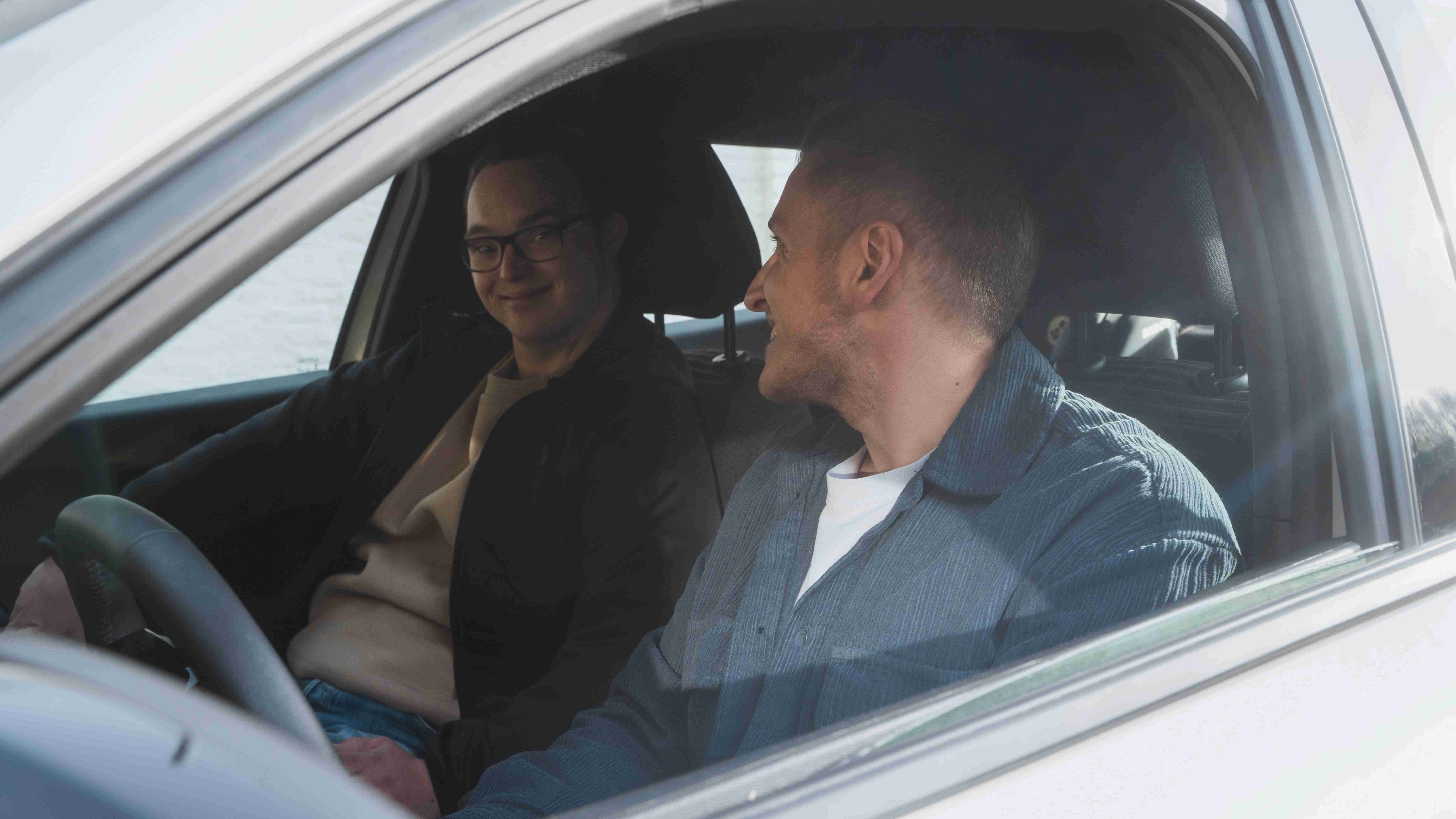 Ist ein Auto sinnvoll? Zwei junge Männer sitzen in einem Auto und lächeln sich an