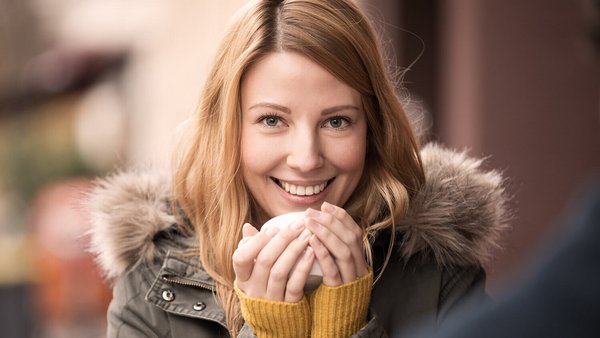 Une jeune femme vêtue d’un manteau se réchauffe avec une tasse - assurance accidents et protection contre le cambriolage pendant la saison sombre 