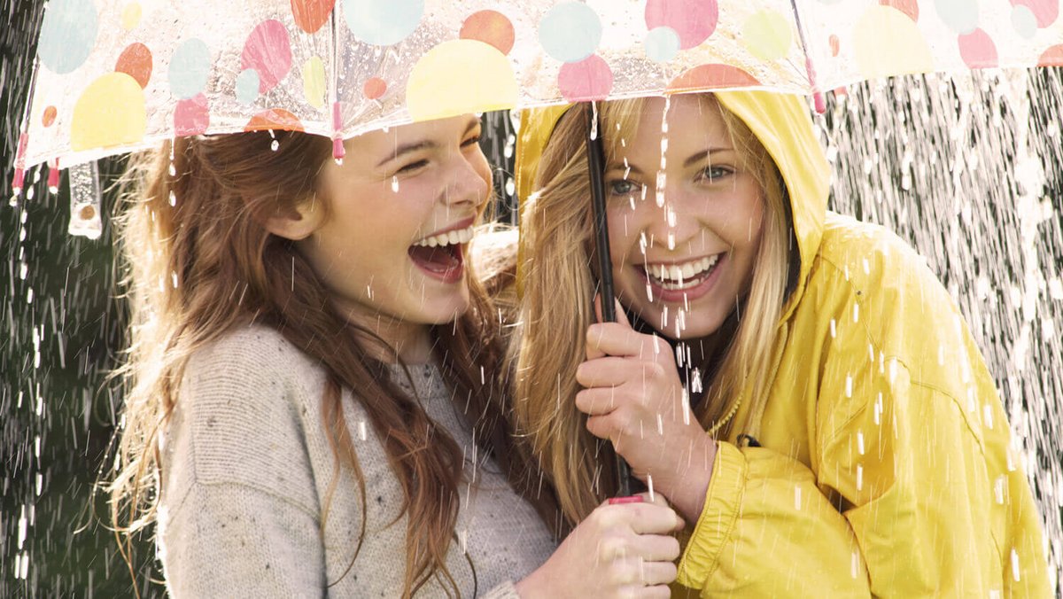 Zwei junge Frauen lachend unter einem Regenschirm