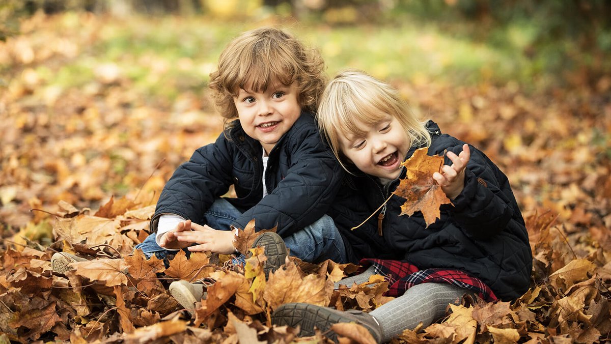 Deux enfants assis sur un parterre de feuilles d’automne