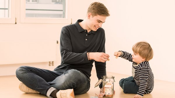 Un enfant et un jeune homme épargnent de l’argent dans un pot