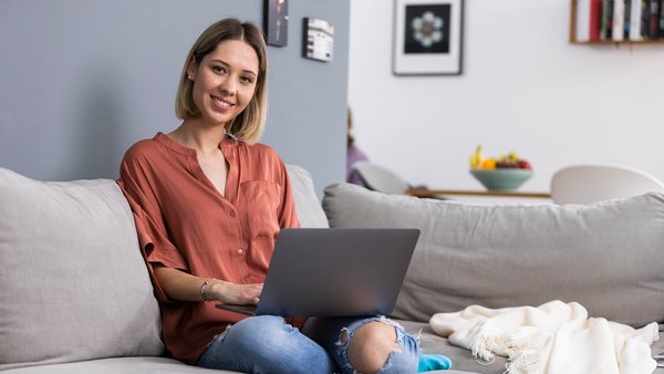 Frau arbeitet zu Hause mit einem Laptop auf der Couch Frau arbeitet zu Hause mit einem Laptop auf der Couch